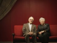 Devoted senior couple sitting together on red sofa — Stock Photo