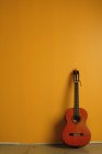 Vintage acoustic guitar standing beside yellow wall — Stock Photo