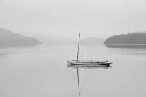 Solitary sailboat reflected in misty lake — Stock Photo