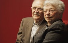Zufriedenes Seniorenpaar blickt in die Kamera auf rotem Hintergrund — Stockfoto
