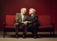 Присвячена старша пара сидить разом на червоному дивані — стокове фото