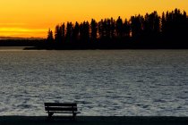 Sonnenuntergang und Bank am Ufer — Stockfoto