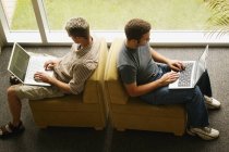 Dos hombres trabajando con ordenadores portátiles en casa - foto de stock