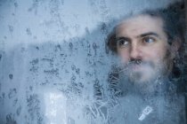 Молодой человек смотрит в замороженное окно — стоковое фото