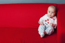 Bébé fille assis sur le canapé rouge — Photo de stock