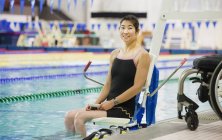 Paraplegic woman sitting at edge of swimming pool on lift — Stock Photo