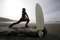 Vista lateral del surfista estiramiento en la playa - foto de stock