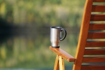 Taza de café en silla de cubierta contra fondo borroso - foto de stock