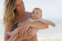 Caucasiano mãe segurando bebê menina na praia — Fotografia de Stock