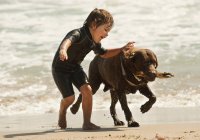 Ein Junge läuft mit einem Hund am Strand von dos stuten vor dem hotel dos stuten; tarifa, cadiz, andalusien, spanien — Stockfoto