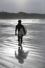 Vista trasera del surfista caminando en la playa - foto de stock