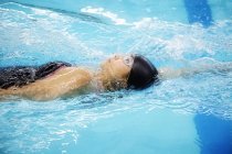 Woman wearing cap and goggles swimming backstroke — Stock Photo