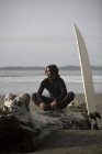 Surfer sitzt auf Baumstamm am Strand, Cox Bay bei Tofino, britisch col — Stockfoto