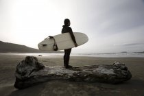 Surfista en la playa con tabla en la mano en la orilla - foto de stock