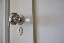 Una maniglia di cristallo e un buco della serratura su una porta bianca — Foto stock