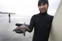 Серфер держит в руках морскую звезду на пляже — стоковое фото