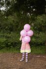 Menina segurando balões rosa na frente da cara — Fotografia de Stock