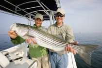 Two men holding a fresh caught striped bass — Stock Photo