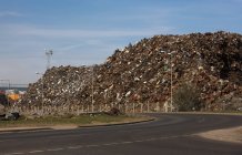 Ferro-velho com pilha de lixo de metal ao lado da estrada — Fotografia de Stock