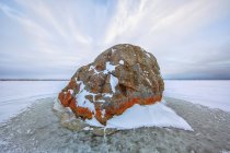 Large lichen covered rock in frozen lake — Stock Photo