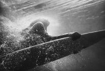 Mujer sobre tabla de surf bajo el agua, imagen monocromática - foto de stock
