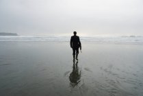 Vue arrière de l'homme sur la plage mouillée tenant un parapluie — Photo de stock