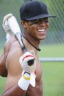 Молодой взрослый мультирасовый мужчина с бейсбольной экипировкой улыбается в камеру — стоковое фото
