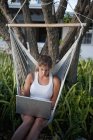 Menina trabalhando em um laptop enquanto sentado em uma rede — Fotografia de Stock