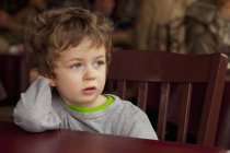Criança menino sentado na cadeira do restaurante olhando para fora — Fotografia de Stock