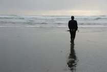 Visão traseira do homem na praia molhada segurando um guarda-chuva — Fotografia de Stock