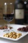 Verre de vin rouge présenté sur un plateau avec une variété de noix — Photo de stock