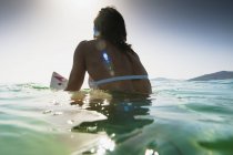 Visão traseira da mulher sentada na prancha de surf na água — Fotografia de Stock