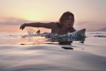 Woman laying on surfboard and watching sunset — Stock Photo