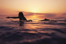 Жінка лежить на дошці для серфінгу і дивиться захід сонця — стокове фото