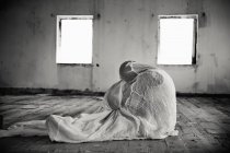 Человек, завернутый в одеяло в пустой комнате, монохромный — стоковое фото