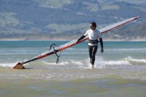 Windsurfer latino che trasporta tavola da surf sulla spiaggia — Foto stock