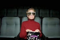 Mature woman sitting in movie theater with popcorn — Stock Photo