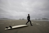 Surfeur s'étirant sur la plage à côté de la planche de surf — Photo de stock