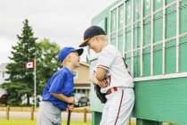 Two boys in baseball uniforms playfully argue in front of the scoreboard during a baseball game at a sports field; Fort McMurray, Alberta, Canada — Stock Photo