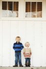 Young boy and girl standing side by side against a white wall — Stock Photo
