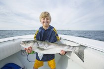 Jovem menino segurando grande Striped Bass em barco de pesca ao largo da costa atlântica, Boston, Massachusetts, Estados Unidos da América — Fotografia de Stock