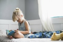 Menina sentada em sua cama lendo uma Bíblia infantil; Langley, British Columbia, Canadá — Fotografia de Stock