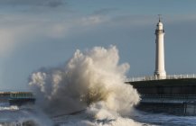 Wave breaks in front of a lighthouse — Stock Photo
