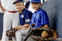 A closeup focus on a game used baseball and glove with young boy players in uniform sitting on the dugout bench in the background; Fort McMurray, Alberta, Canada — Stock Photo