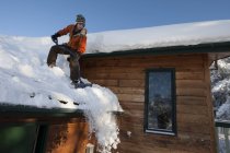 Young woman removing snow from the roof of house — Stock Photo