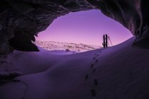 Empreintes de pas conduisent vers un splitboard placé à l'entrée d'une grotte de glace dans le glacier Canwell en Alaska Range après le coucher du soleil en hiver, Alaska, États-Unis d'Amérique — Photo de stock