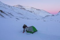 Homem que monta a barraca após o por do sol durante uma viagem de acampamento do inverno na escala de Alaska, perto da geleira de Augustana, Alaska, Estados Unidos da América — Fotografia de Stock
