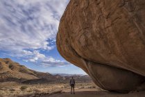 Man standing under huge boulder — Stock Photo