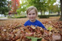 Giovane ragazza seduta in mucchio di foglie in autunno — Foto stock