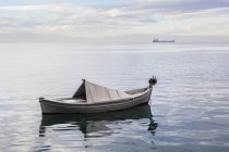 Um barco flutuando no tranquilo Mar Egeu com um navio no di — Fotografia de Stock